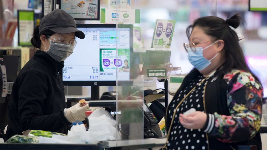A grocery store worker wears a protective face mask and gloves as a customer stands on the other side of the plexiglass divider in downtown Vancouver Wednesday, April 29, 2020. THE CANADIAN PRESS/Jonathan Hayward