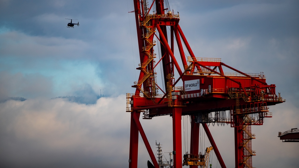 A helicopter preparing to land at a helipad on the harbour passes a gantry crane used to load and unload container ships at port, in Vancouver, on Monday, Dec. 28, 2020. (Darryl Dyck / THE CANADIAN PRESS)