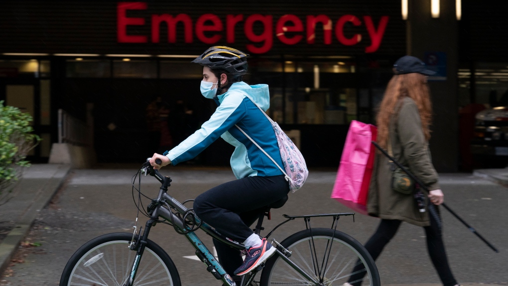 A woman wears a protective face covering to help prevent the spread of COVID-19 as she bikes past the emergency entrance of Vancouver General Hospital in Vancouver, B.C., Friday, April 9, 2021. THE CANADIAN PRESS/Jonathan Hayward