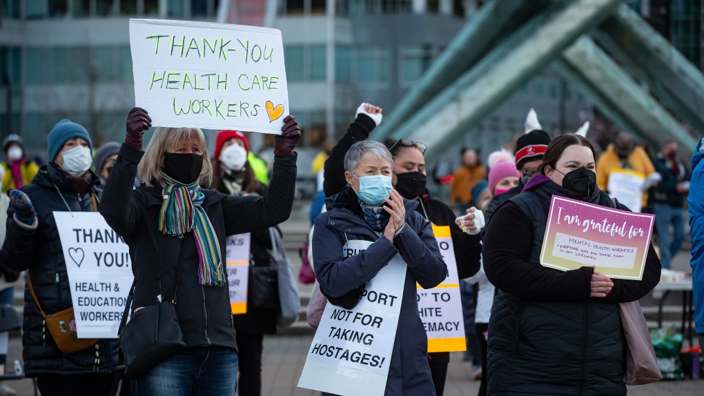 People applaud and hold signs during a 'gratitude gathering' to recognize COVID-19 pandemic heroes, including healthcare workers and teachers, in Vancouver, Monday, Feb. 21, 2022. (Darryl Dyck / THE CANADIAN PRESS)