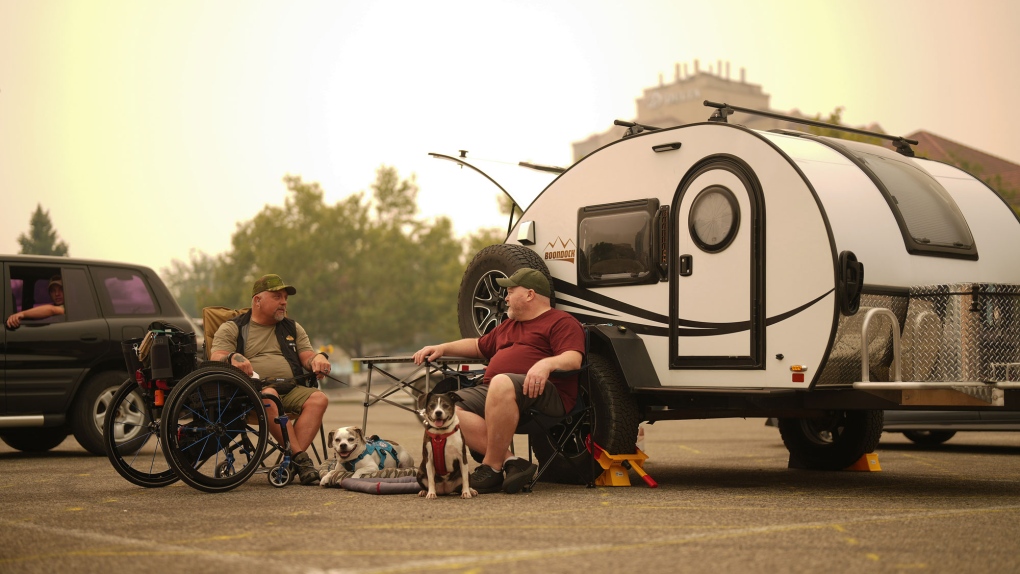 FILE: Wildfire evacuees Rob Pullen, left, and Warren Pullen sit with their dogs outside their trailer in the parking lot at an evacuation centre in Kelowna, B.C., on Aug. 19, 2023. (THE CANADIAN PRESS/Darryl Dyck)