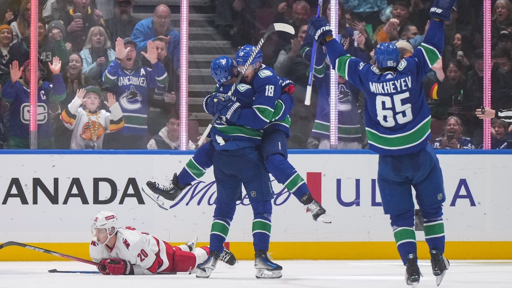 Vancouver Canucks' Sam Lafferty (18) leaps into the arms of Elias Pettersson as they and Ilya Mikheyev (65) celebrate Pettersson's goal while Carolina Hurricanes' Sebastian Aho (20) lies on the ice during the third period of an NHL hockey game in Vancouver, on Saturday, December 9, 2023. THE CANADIAN PRESS/Darryl Dyck